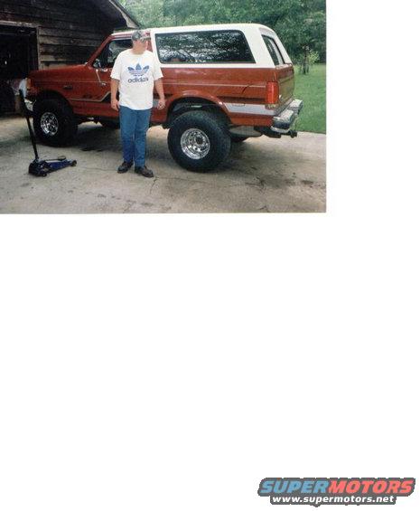 Man standing next to a red and white 1987 Ford Bronco with aftermarket wheels