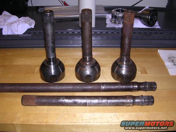 Axle shafts and CV joints on a wooden surface. Supermotors.net logo visible