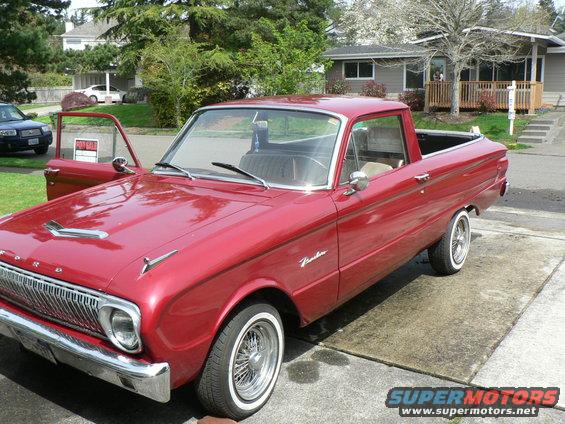 Red 1960s pickup truck with whitewall tires and chrome wire wheels, driver's door open