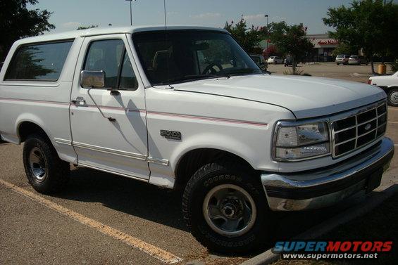 White Ford Bronco parked in a lot, front 3/4 view. Red pinstripe detail on side