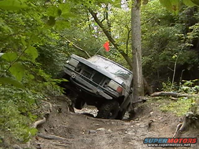 Dark gray Ford Bronco off-roading on a dirt trail, angled up a steep incline