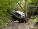 1988 Ford Bronco - A dark gray Ford Bronco navigates a challenging off-road trail, climbing a steep, muddy incline.