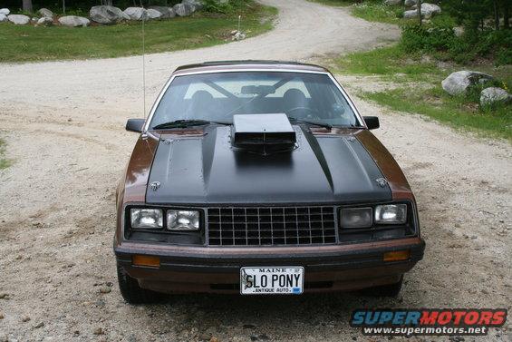 Brown and black 1979 Ford Mustang with a hood scoop, parked on a dirt road