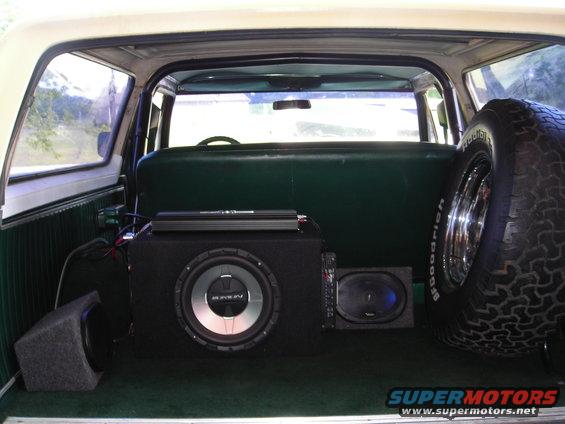 Interior view of a 1979 Ford Bronco showing aftermarket subwoofers, amplifier, and spare tire