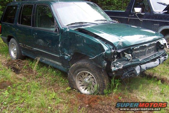 Damaged green SUV with flat front tire, parked next to a dark pickup truck
