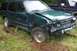 2004 Arctic Cat F-7 Firecat - This green SUV has significant front-end damage and a flat tire, parked in a grassy area next to another vehicle.