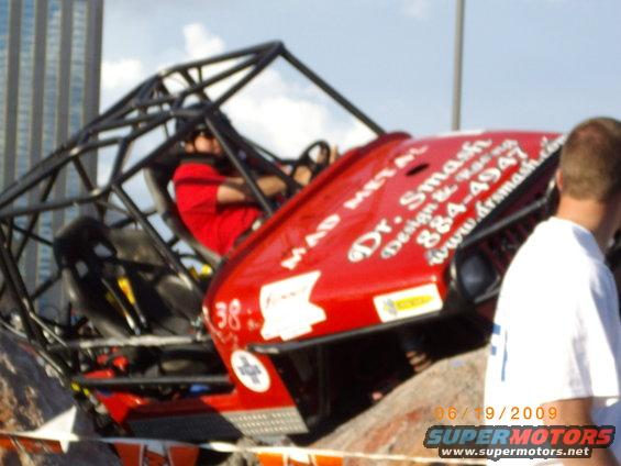 Red off-road buggy with a roll cage, driven by a person in a red shirt. Text on the side reads 'Dr. Smash'