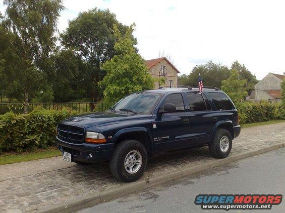 Dark blue SUV with an American flag on the roof rack, parked curbside