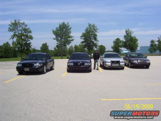 Four police interceptor sedans parked in a lot with a guy standing between two of them