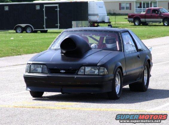 Black drag car with a large hood scoop, driver in helmet, on a track