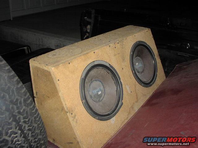 Wooden box with two large speakers, partially visible tire and car body