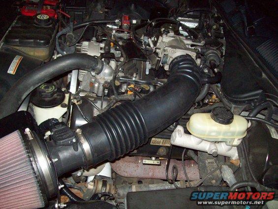 Engine bay showing a large black intake tube connected to a cone air filter, with various engine components visible