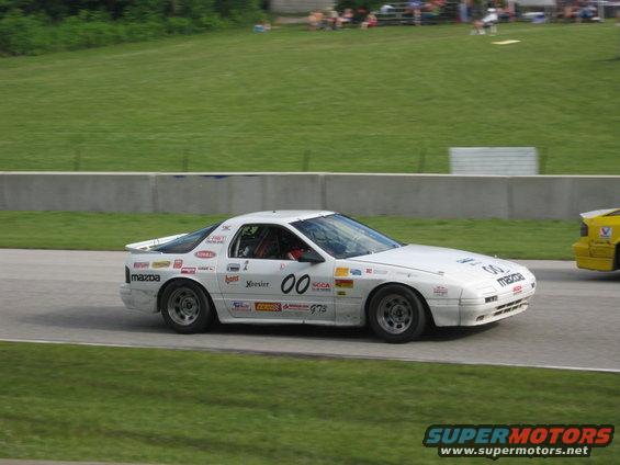 White Mazda RX-7 race car with number 00 on side, driving on track