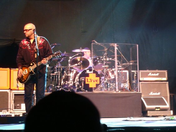 Musicians performing on stage with drums and amplifiers, a guitarist in the foreground