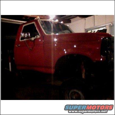 Red pickup truck in a garage, possibly undergoing repairs. The front end is partially visible