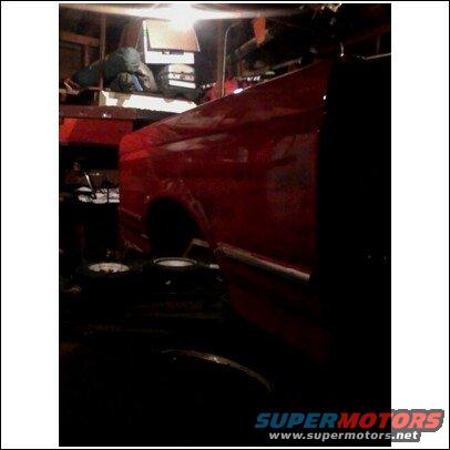 Red truck bed and fender in a dimly lit garage, showing a chrome trim piece and wheel well