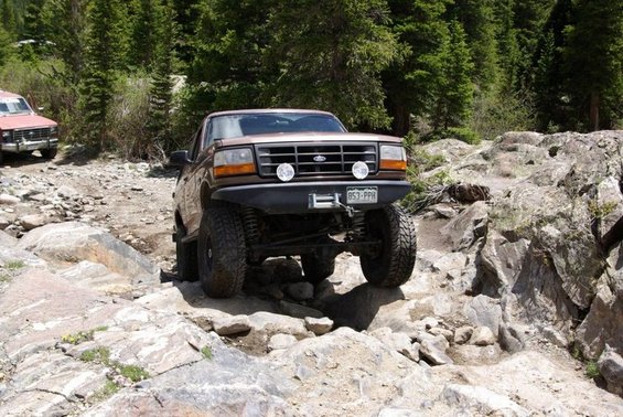 Brown Ford Bronco navigating rocky terrain, front bumper with winch and lights, Colorado license plate 853-PPH