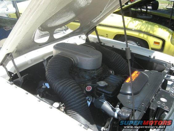 Engine bay with large black air intake hoses and a yellow car in the background