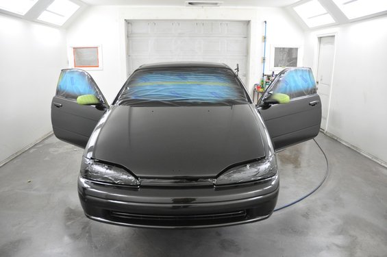 Dark sedan with doors open, windows taped off for painting