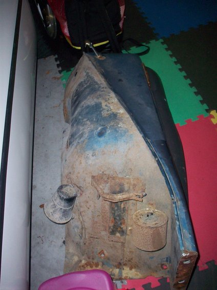Rusted blue vehicle fender with some attached metal brackets and a cylindrical component