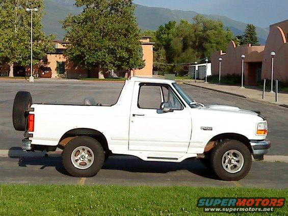 White 1995 Ford Bronco parked on grass, side view, with spare tire mounted on rear