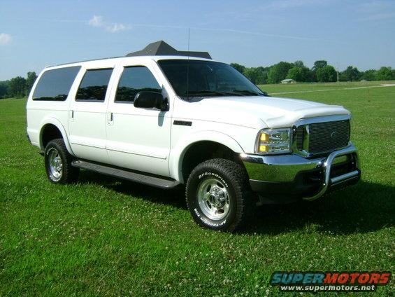 White 2000 Ford Excursion parked on a grassy field, front-right quarter view, with chrome bull bar and tinted windows
