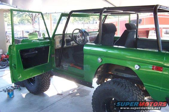 Green 1976 Ford Bronco with doors open, showing interior and roll cage