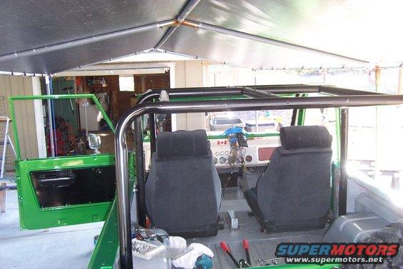 Green 1976 Ford Bronco interior with roll cage, black seats, and dashboard gauges