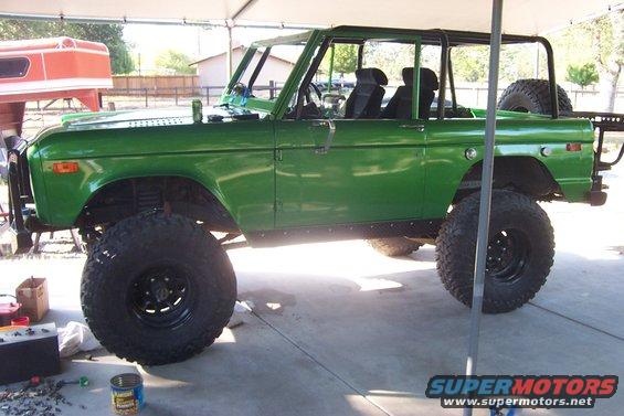 Green 1976 Ford Bronco with lifted suspension and large tires, parked under a canopy
