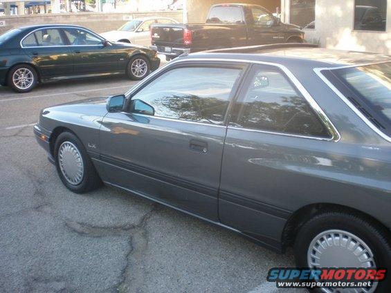 1989 Mazda MX-6 coupe, side view. Another car and a truck are parked nearby