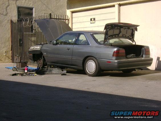 Gray 1989 Mazda MX-6 coupe with hood and trunk open, front wheel removed for repairs