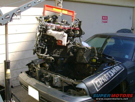 Engine being lifted out of a car with an engine hoist. Craftsman logo visible on fender