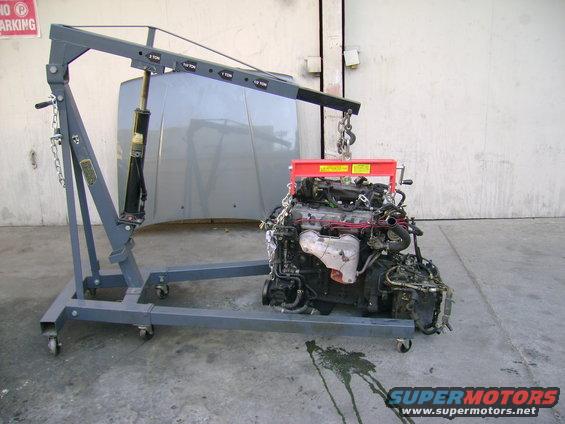 Engine hoist lifting a car engine, with a car hood in the background