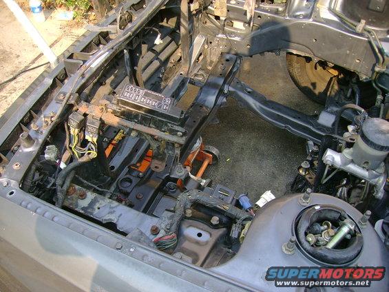 Car engine bay showing fuse box, wiring harnesses, and master cylinder