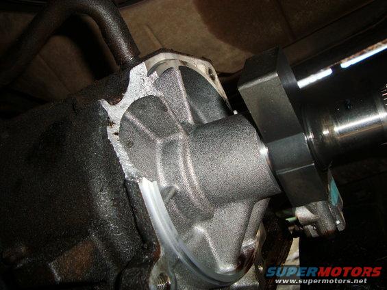 Close-up of a gray metal drivetrain part with oil residue, showing a cut edge and a shaft extending to the right
