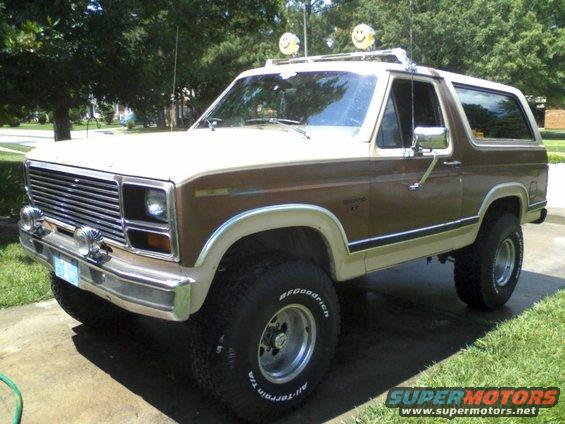 1986 Ford Bronco with two-tone brown and tan paint, lifted suspension, and roof rack with smiley face lights