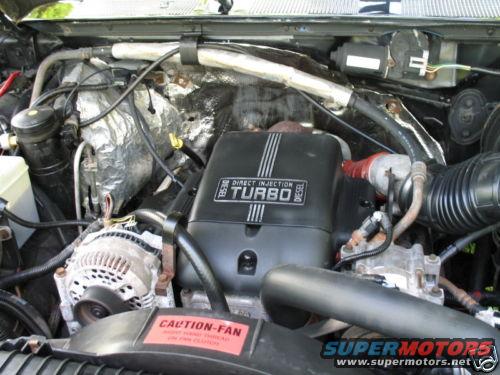 Engine bay with black "DIRECT INJECTION TURBO DIESEL" cover, alternator, and red "CAUTION-FAN" sticker