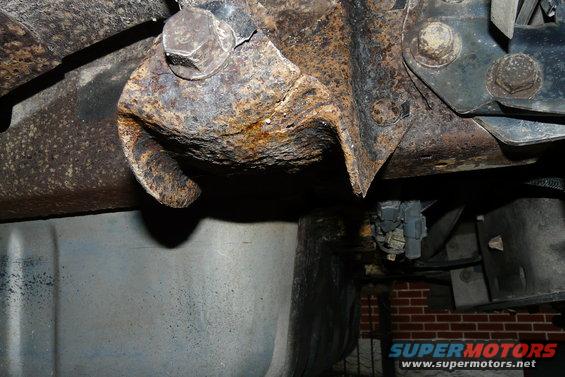 Heavily rusted metal frame and suspension components of an undercarriage. Visible bolts and brackets show significant corrosion