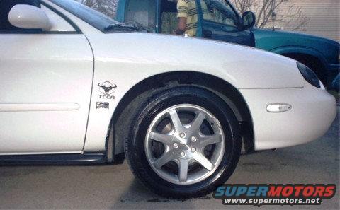 White sedan fender with bull decal and alloy wheel; other vehicles in background