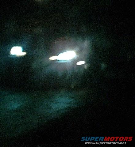 Car headlights glowing in the dark, with a watermark for Supermotors.net at the bottom right