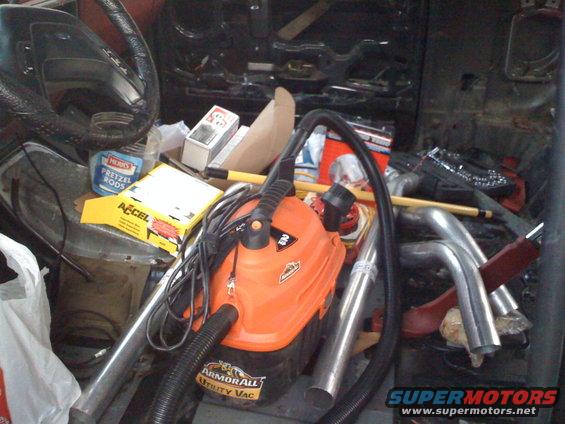 Interior of a vehicle packed with an orange shop vac, boxes, and exhaust pipes