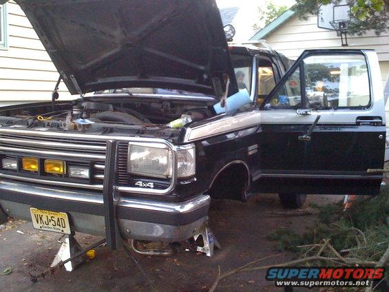 1988 Ford Bronco front end with hood open, driver door ajar, on jack stands