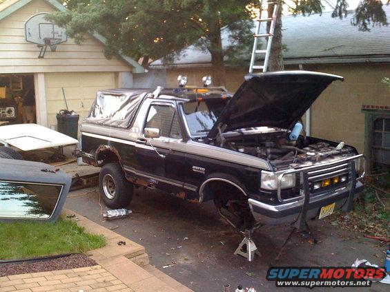 Black Ford Bronco on jack stands with hood open, undergoing repairs in a driveway