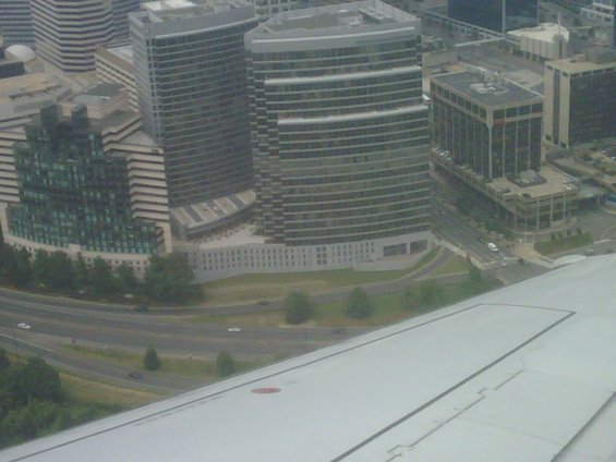 Aerial view of modern office buildings and a highway, with an airplane wing in the foreground