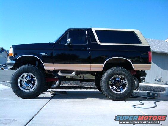 Lifted 1994 Ford Bronco, black with tan trim, custom chrome wheels, side view