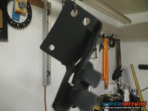 Black metal bracket hanging in a workshop, with tools and supplies in the background
