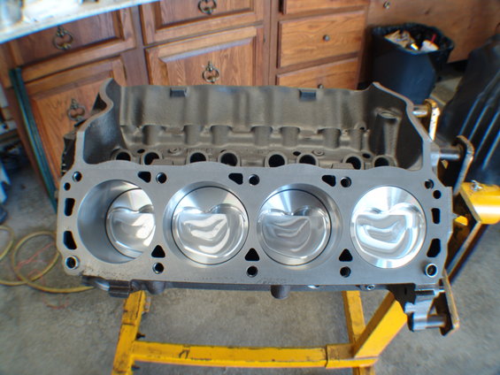 Engine block with four polished pistons, mounted on a yellow stand