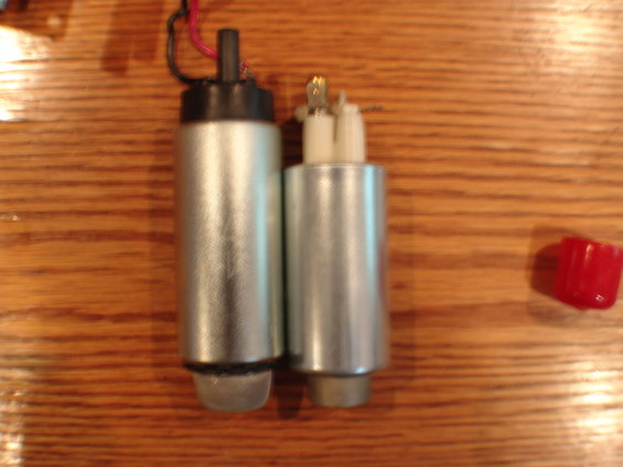 Two silver fuel pumps with electrical connectors and a red cap on a wooden surface
