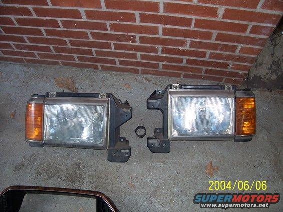 Pair of used Ford Bronco headlights, one with a broken mounting bracket, on concrete floor