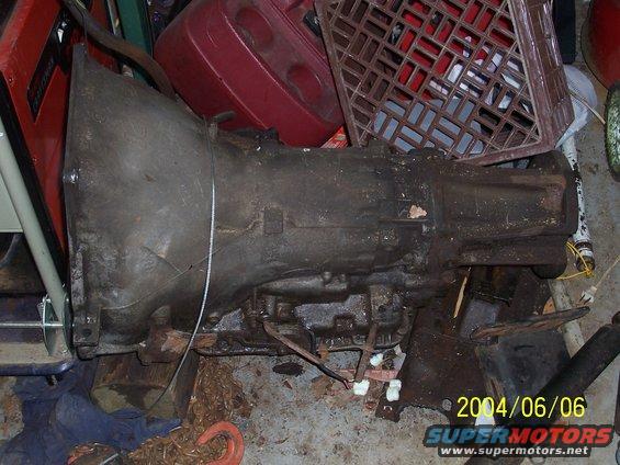 Old automatic transmission, looks like it's seen better days. Some red plastic and a crate are behind it